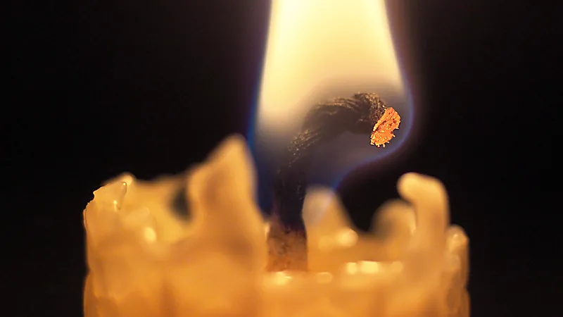Close-up of a burning candle wick curled over with a glowing carbon tip inside the flame