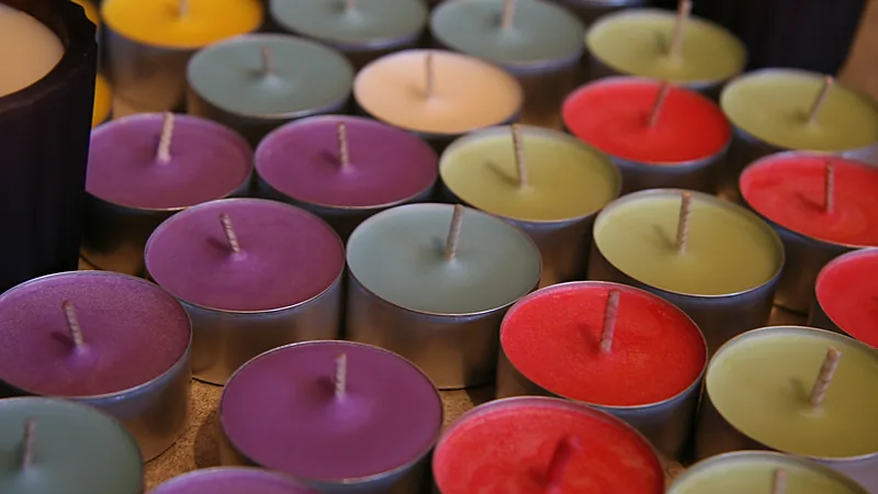 Rows of colorful tealight candles in metal cups, each with a short cotton wick