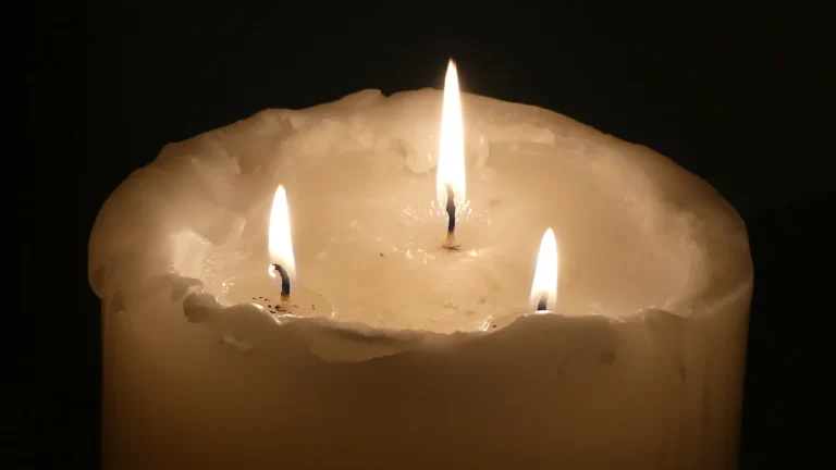 Large white pillar candle burning with three wicks and a wide pool of melted wax