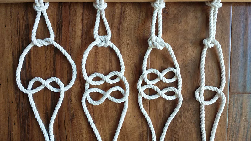 Four white cotton cords hanging from a dowel, each tied with different knots below the mounting loops