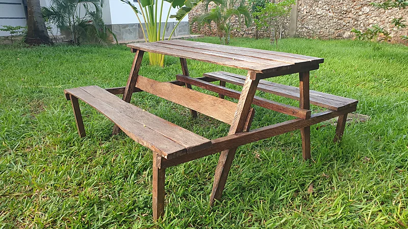 Homemade wooden picnic table with attached benches in a dark brown finish, standing on grass