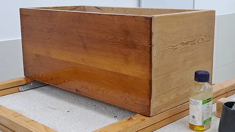 Pine wood box with a fresh oil finish showing warm amber grain, next to a small bottle of linseed oil
