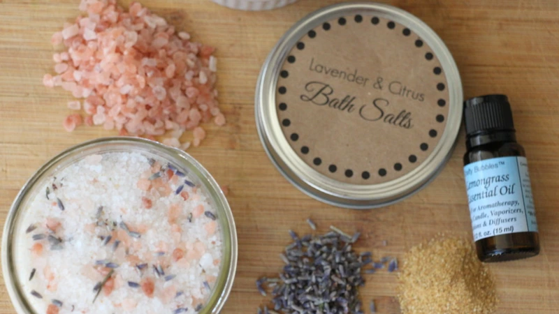 Flat lay on a wooden board of a jar of bath salts, loose pink Himalayan salt, dried lavender, sugar, an essential oil bottle and a kraft paper labelled lid