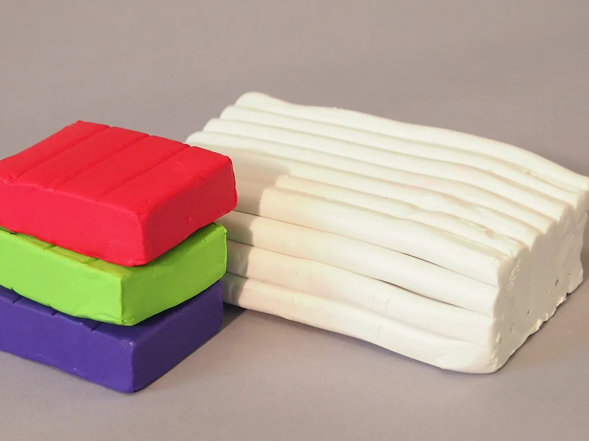 Three blocks of coloured polymer clay stacked beside a larger block of white clay on a grey surface