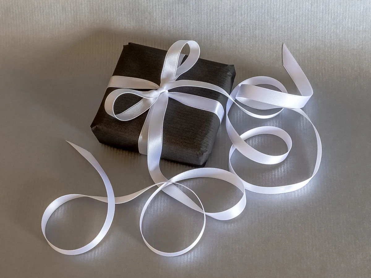Black wrapped parcel tied with a long white silk ribbon trailing in loops