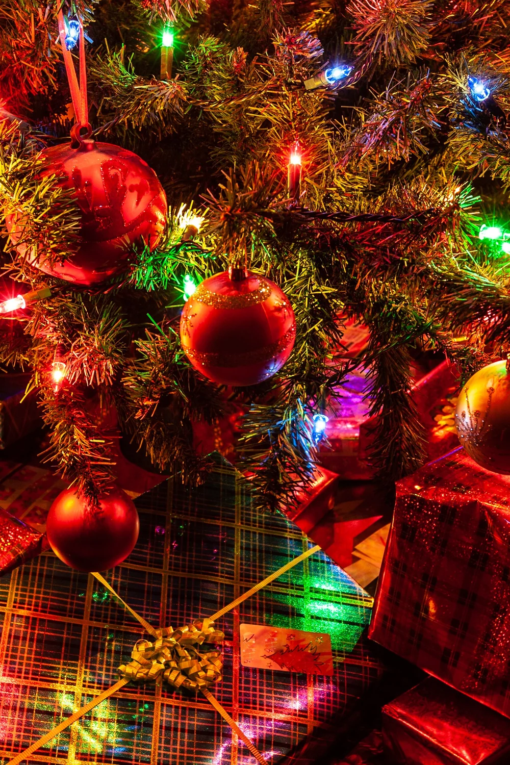 Christmas tree decorated with red and gold baubles and coloured lights above wrapped presents