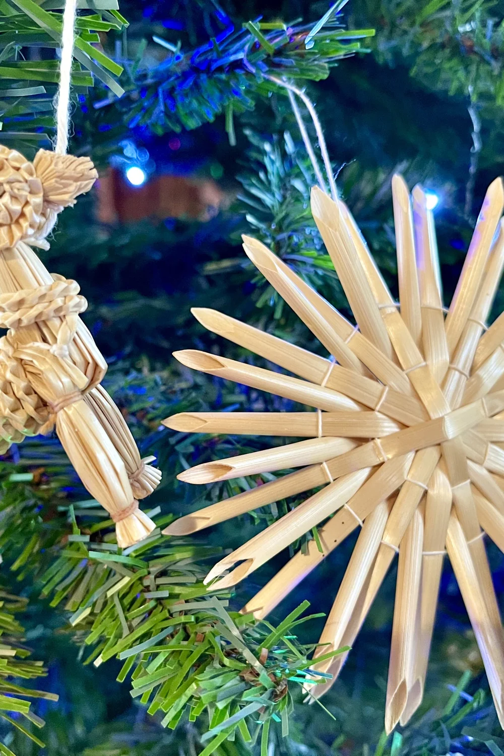 Woven straw reindeer and straw star ornaments hanging on a Christmas tree