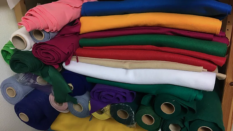 Rolls and folded sheets of craft felt in many colours stacked on a shelf