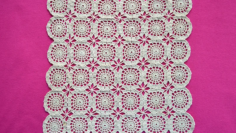 Crocheted runner made of joined square motifs in cream cotton on a magenta background