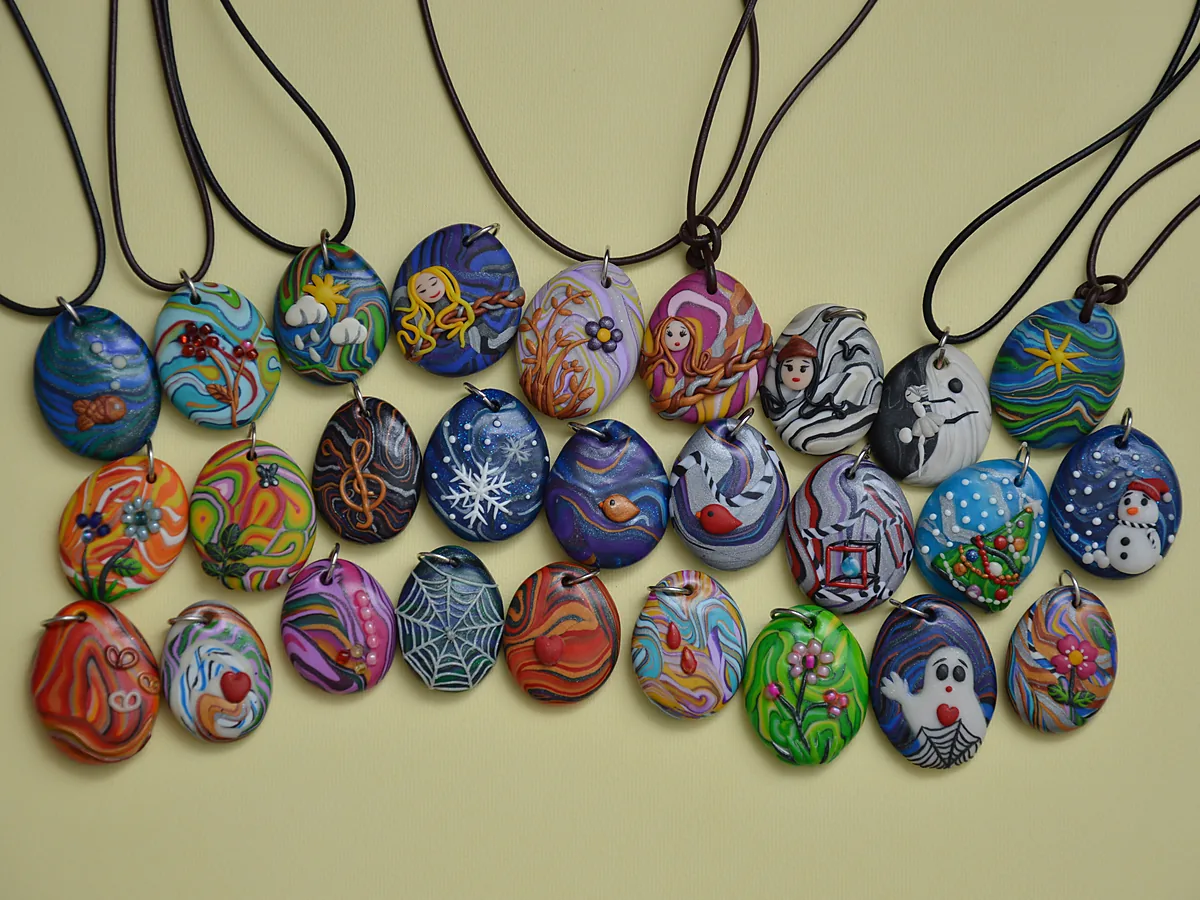 Rows of oval polymer clay pendants on leather cords, each patterned with swirls, flowers and small figures