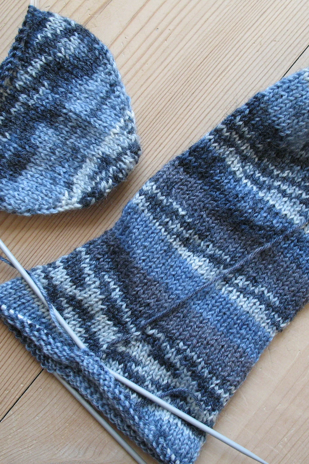 Knitted sock and one in progress on double-pointed needles on pale wood