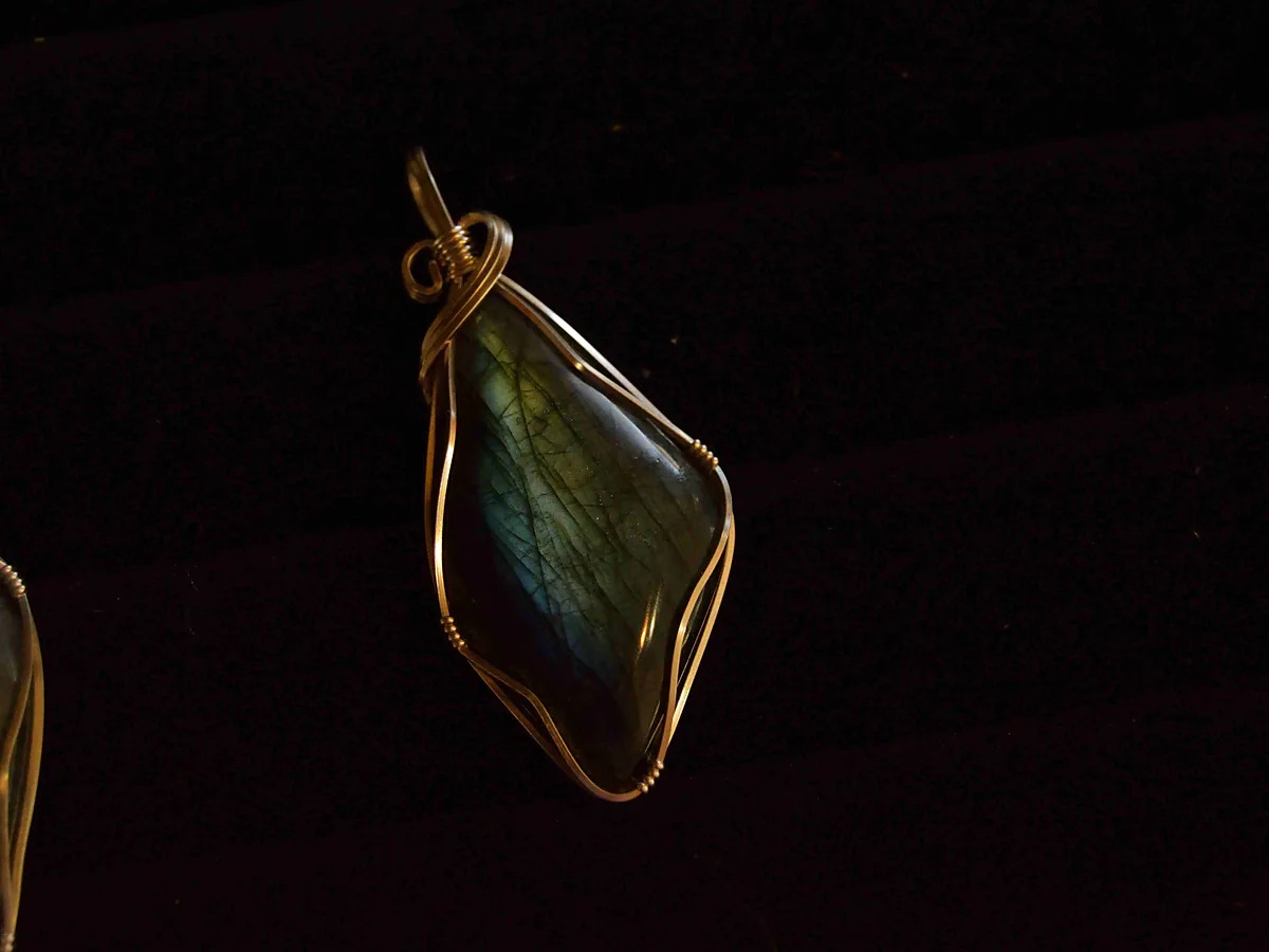 Wire-wrapped labradorite pendant held in a gold wire cage against a dark background