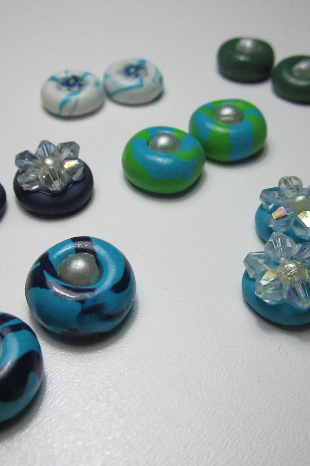 Round polymer clay stud earrings in blue, green and navy, some set with a pearl bead and some with clear crystals