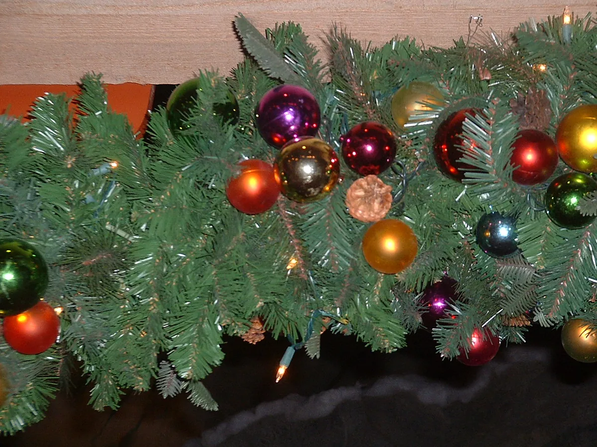 Faux evergreen garland draped along a shelf with coloured glass baubles and white string lights