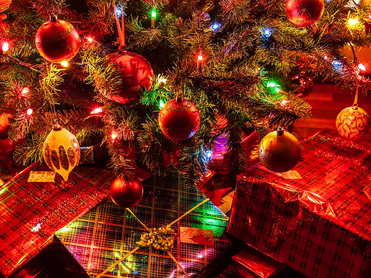 Red and gold baubles with coloured string lights on a Christmas tree above wrapped presents