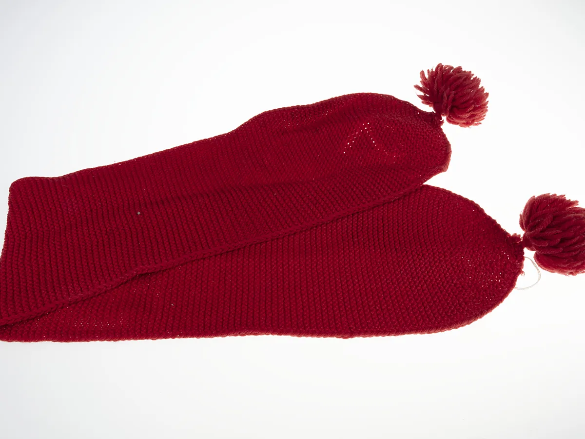 Red knitted scarf with pom-poms at each end, laid flat