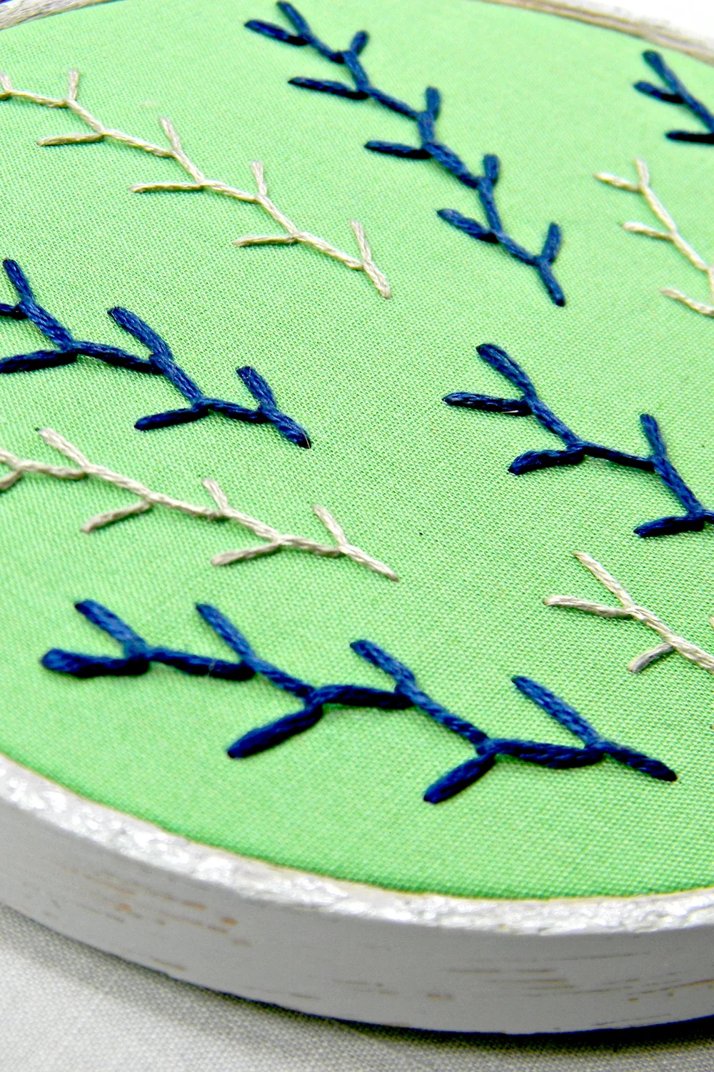 Hand-embroidered hoop art with blue and cream feather stitch on green fabric
