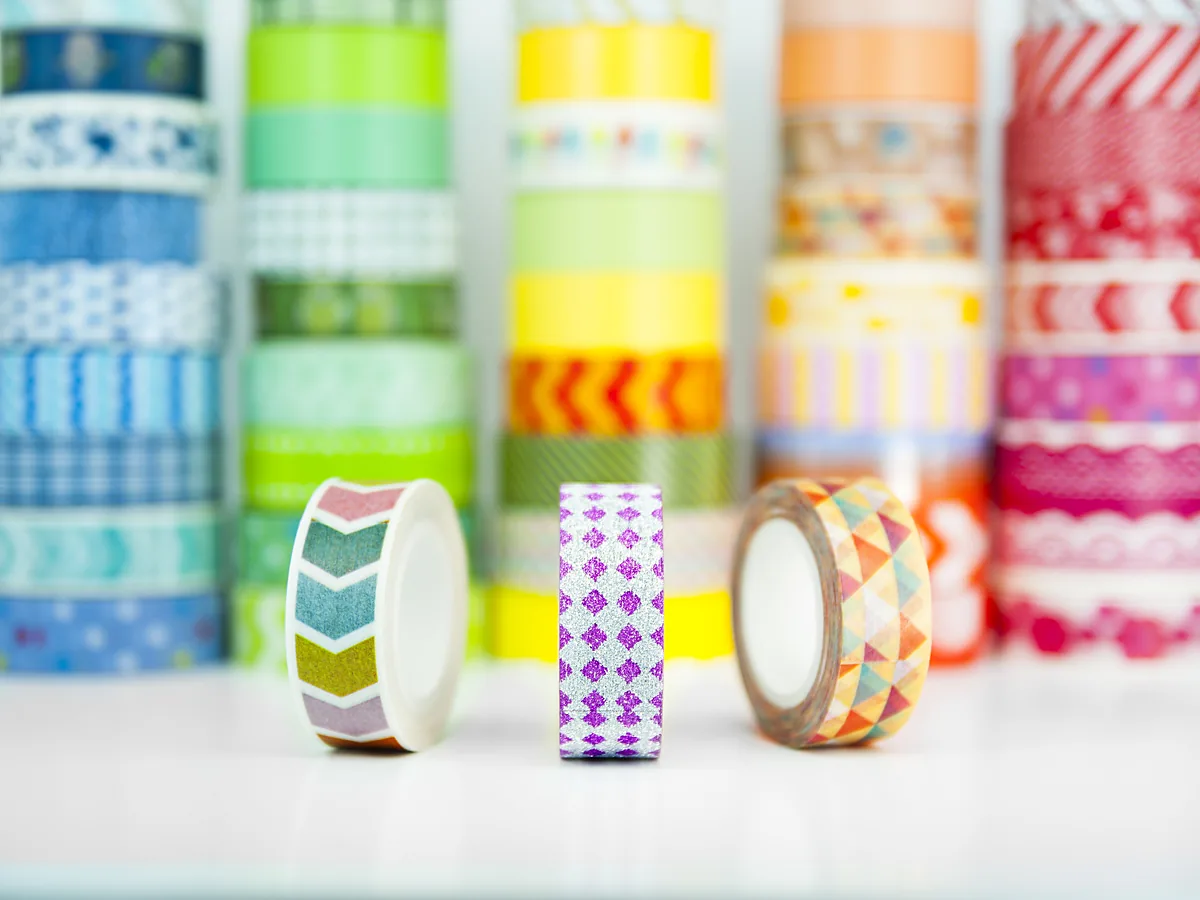 Rolls of patterned washi tape in several colours arranged on a white surface